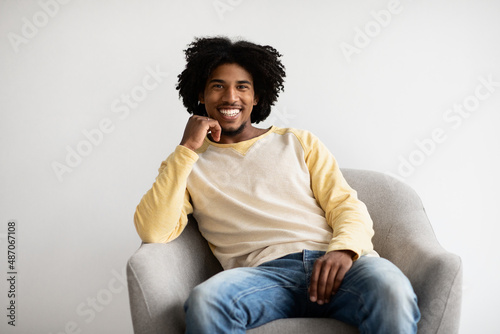 Handsome Young Black Guy Sitting In Armchair And Smiling To Camera