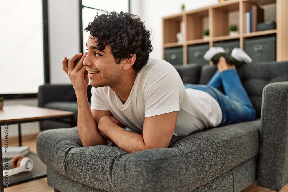 Young hispanic man talking on the smartphone lying on the sofa at home. Young hispanic man talking on the smartphone lying on the sofa at home.