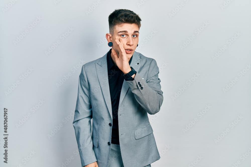Young caucasian boy with ears dilation wearing business jacket hand on mouth telling secret rumor, whispering malicious talk conversation Young caucasian boy with ears dilation wearing business jacket hand on mouth telling secret rumor, whispering malicious talk conversation
