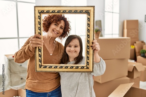 Mature mother and down syndrome daughter moving to a new home, standing by cardboard boxes holding vintage frame