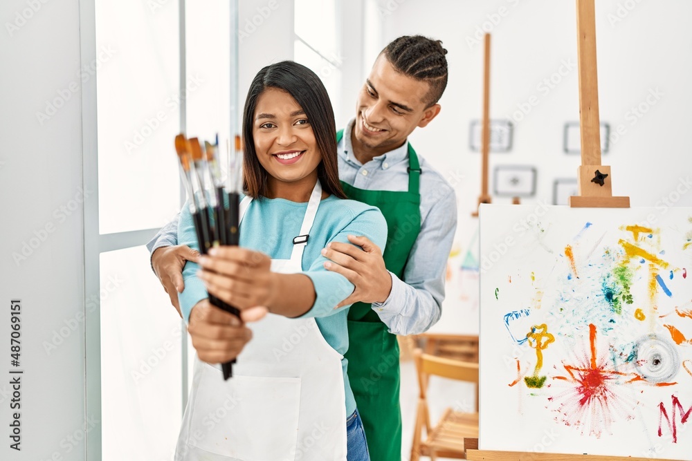 Young latin painter couple smiling happy holding paintbrushes at art studio Young latin painter couple smiling happy holding paintbrushes at art studio