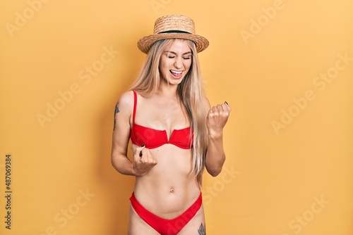Young caucasian woman wearing bikini and summer hat celebrating surprised and amazed for success with arms raised and eyes closed. winner concept.