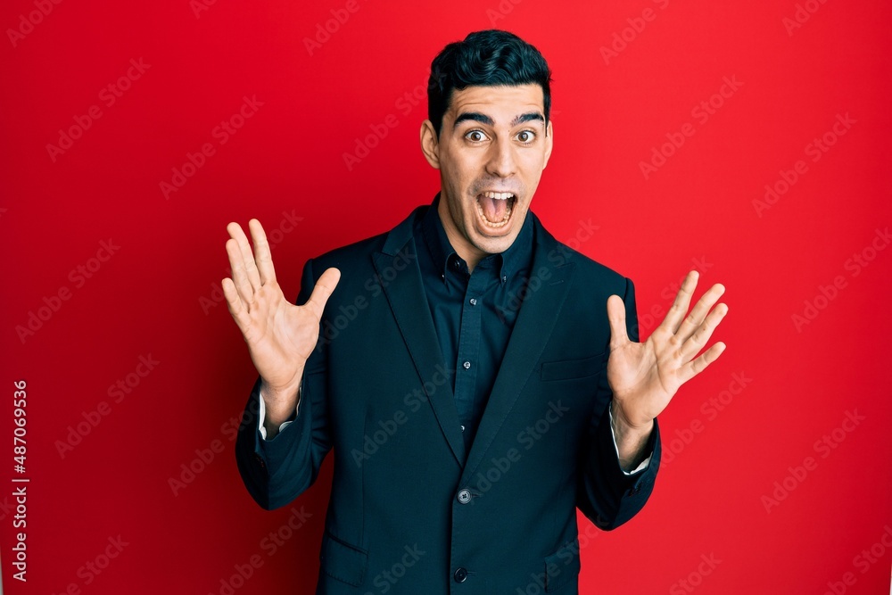 Naklejka premium Handsome hispanic man wearing business clothes celebrating crazy and amazed for success with arms raised and open eyes screaming excited. winner concept
