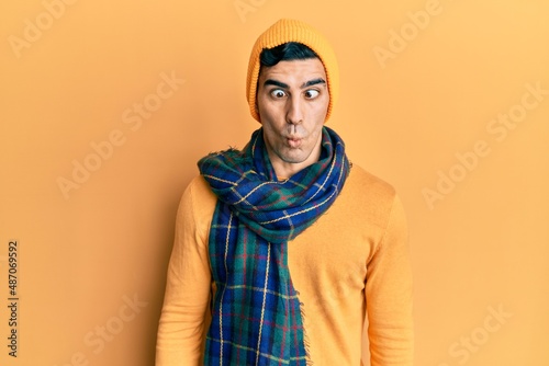 Handsome hispanic man wearing wool hat and winter scarf making fish face with lips, crazy and comical gesture. funny expression. © Krakenimages.com