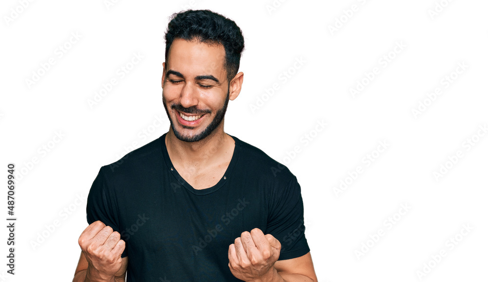Hispanic man with beard wearing casual black t shirt excited for success with arms raised and eyes closed celebrating victory smiling. winner concept. Hispanic man with beard wearing casual black t shirt excited for success with arms raised and eyes closed celebrating victory smiling. winner concept.
