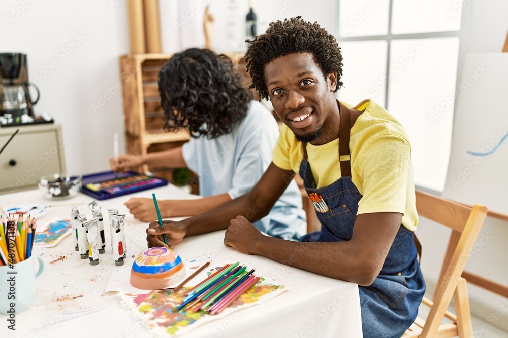 Naklejka premium African american artist couple smiling happy painting sitting on the table at art studio.