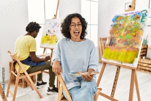 Young hispanic woman at art studio winking looking at the camera with sexy expression, cheerful and happy face.
