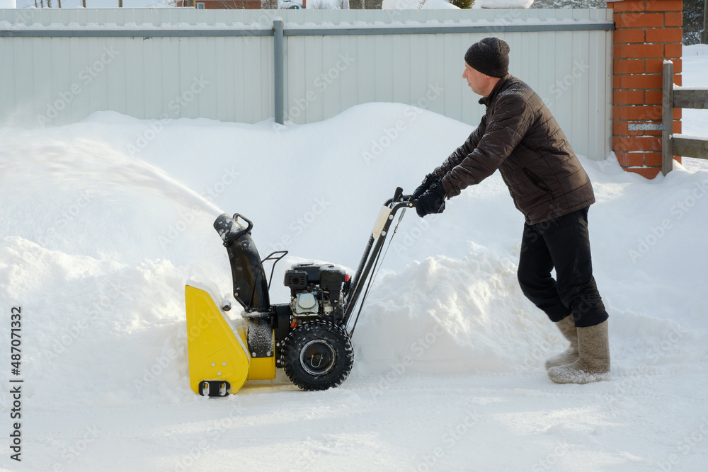 Obraz premium Man using snow plow machine to clear the inner courtyard in winter. Russia.