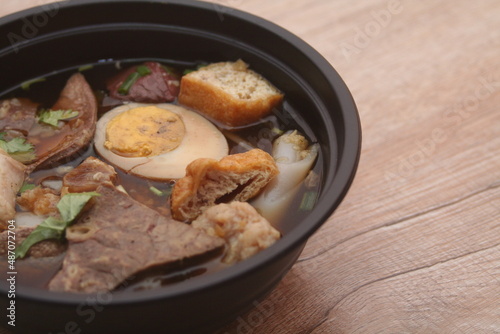 Rolled Rice Noodles in Five-spices Broth or Crunchy Pork Soup, what we call "Noodle and Kuayjub Shop" served in a black bowl.
