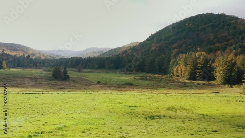 Drone forwarding shot over the hilly terrain covered with green vegetation of trees and grass in Litchfield, Connecticut, United States on a cloudy day. photo