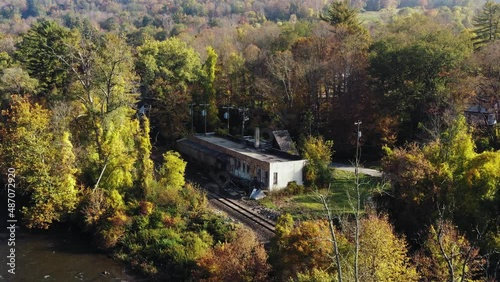 Aerial view of an old house ruin with broken windows beside railway tracks and covered by dense vegetation all around on a summer morning in Litchfield County, Connecticut, United States. photo