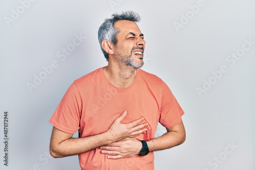 Handsome middle age man with grey hair wearing casual t shirt with hand on stomach because nausea, painful disease feeling unwell. ache concept.