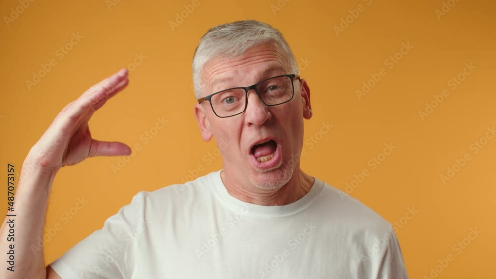 Senior man in glasses doing bla bla gesture against yellow background