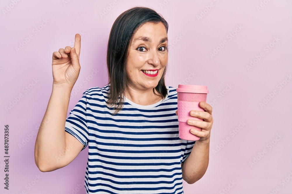 Middle age hispanic woman holding coffee smiling with an idea or question pointing finger with happy face, number one Middle age hispanic woman holding coffee smiling with an idea or question pointing finger with happy face, number one