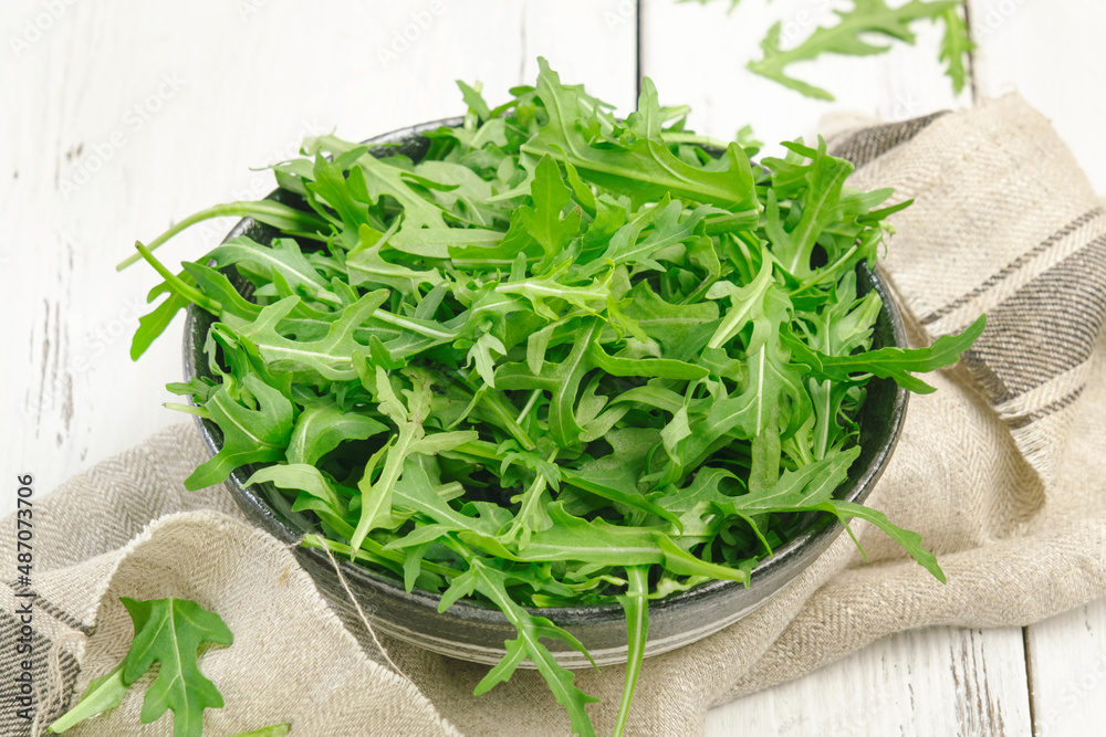 Fresh green arugula in rustic ceramic bowl on white kitchen table background, top view, copy space. Spring spicy herb for healthy eating Fresh green arugula in rustic ceramic bowl on white kitchen table background, top view, copy space. Spring spicy herb for healthy eating