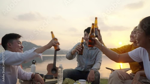 Group Four People Friends Asian men and women Camping, drinking beer, celebrating, Singing, Playing Guitar, Having fun and Enjoying Ground tent. Reservoir area during Sunset Vacation Time.