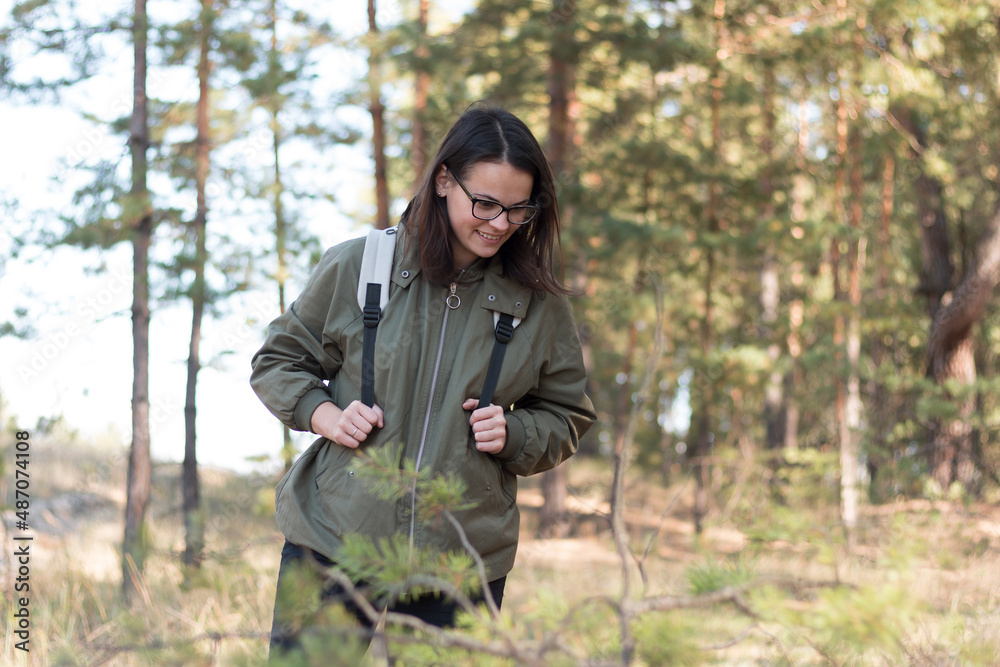 cute girl with dark long hair in glasses looks down standing in the forest with a backpack cute girl with dark long hair in glasses looks down standing in the forest with a backpack