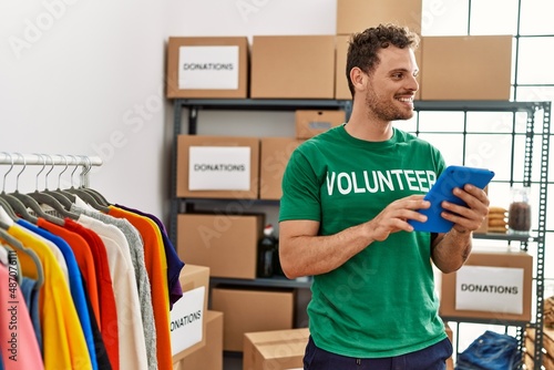 Young hispanic man wearing volunteer uniform using touchpad at charity center