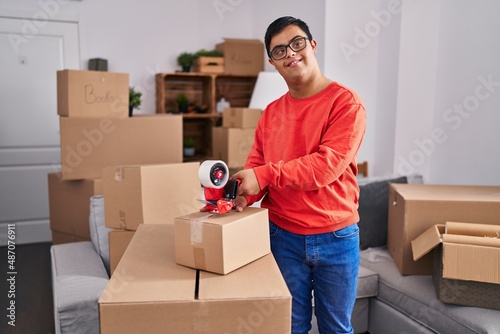 Down syndrome man smiling confident packing cardboard box at new home photo