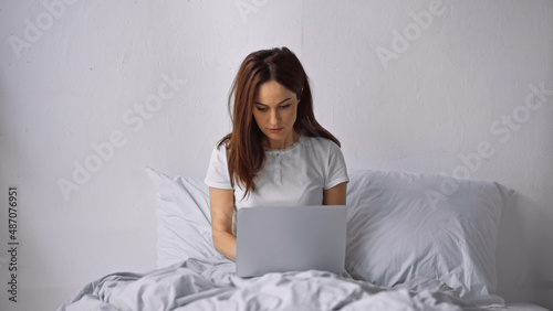 Obraz na plátně brunette woman sitting on bed at home and working on laptop