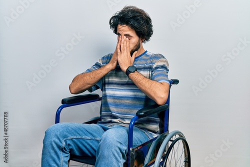 Handsome hispanic man sitting on wheelchair rubbing eyes for fatigue and headache, sleepy and tired expression. vision problem
