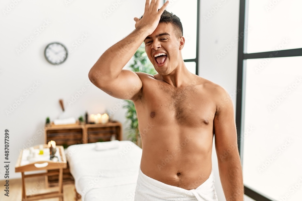 Young hispanic man standing shirtless at spa center surprised with hand on head for mistake, remember error. forgot, bad memory concept. Young hispanic man standing shirtless at spa center surprised with hand on head for mistake, remember error. forgot, bad memory concept.