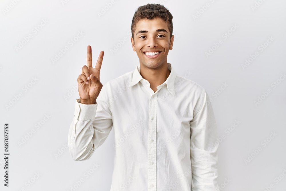 Young handsome hispanic man standing over isolated background showing and pointing up with fingers number two while smiling confident and happy. Young handsome hispanic man standing over isolated background showing and pointing up with fingers number two while smiling confident and happy.