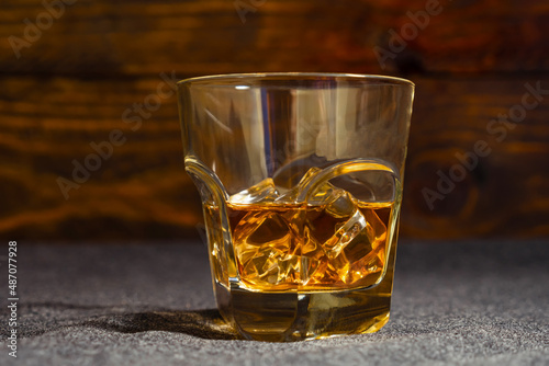 A glass of whiskey on ice against the dark boards. Close-up.