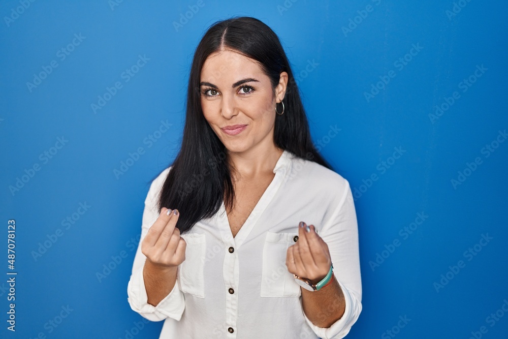 Young hispanic woman standing over blue background doing money gesture with hands, asking for salary payment, millionaire business Young hispanic woman standing over blue background doing money gesture with hands, asking for salary payment, millionaire business