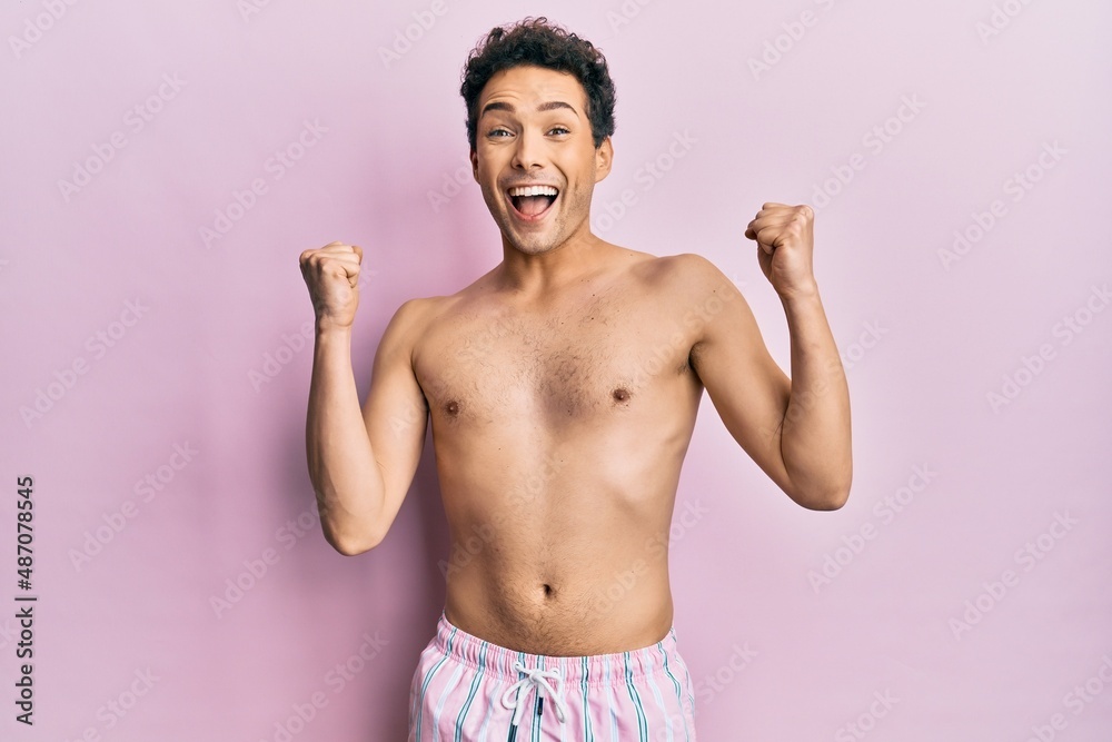 Fototapeta premium Young handsome man wearing swimwear shirtless celebrating surprised and amazed for success with arms raised and open eyes. winner concept.