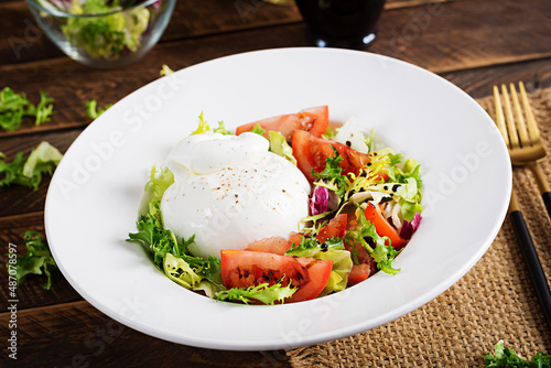 Salad with tomatoes and burrata cheese with lettuce and olive oil on wooden background. Italian cuisine.