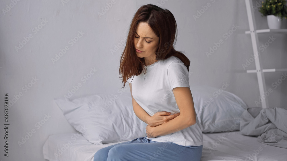 woman sitting on bed and hugging belly while feeling abdominal pain woman sitting on bed and hugging belly while feeling abdominal pain