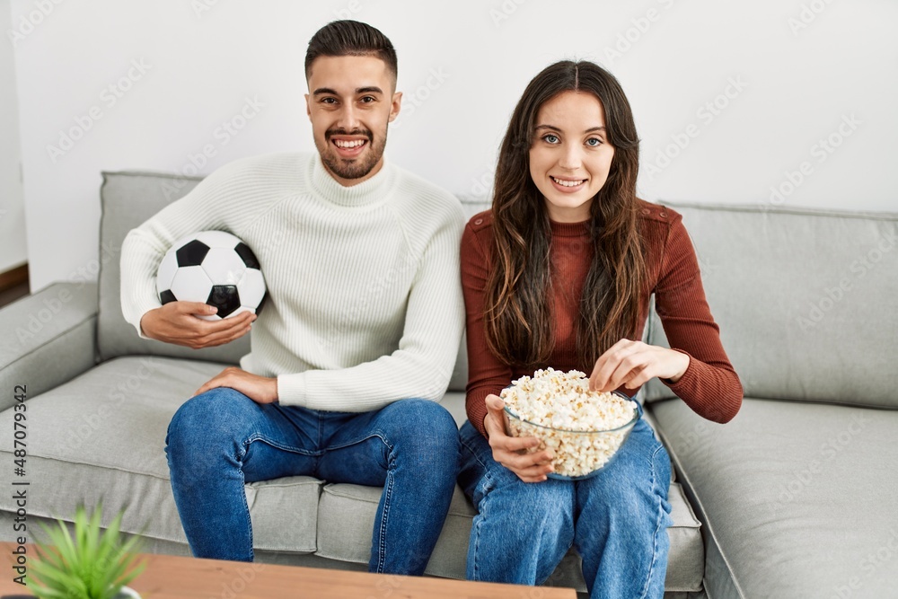 Young hispanic couple watching soccer match eating porpcorn at home. Young hispanic couple watching soccer match eating porpcorn at home.