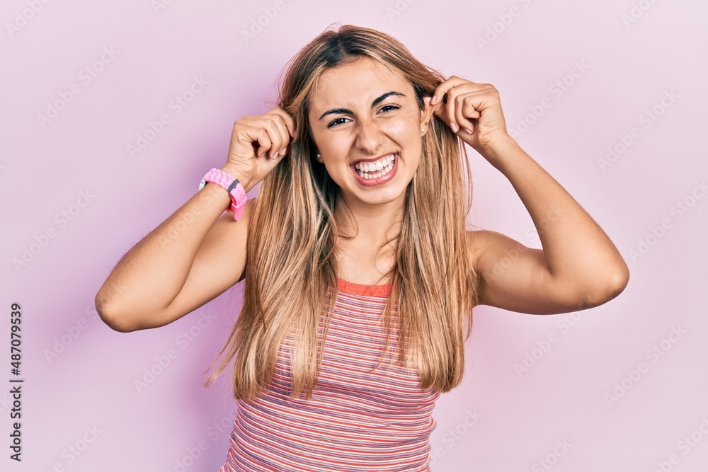 Beautiful hispanic woman wearing casual summer t shirt smiling pulling ears with fingers, funny gesture. audition problem Beautiful hispanic woman wearing casual summer t shirt smiling pulling ears with fingers, funny gesture. audition problem