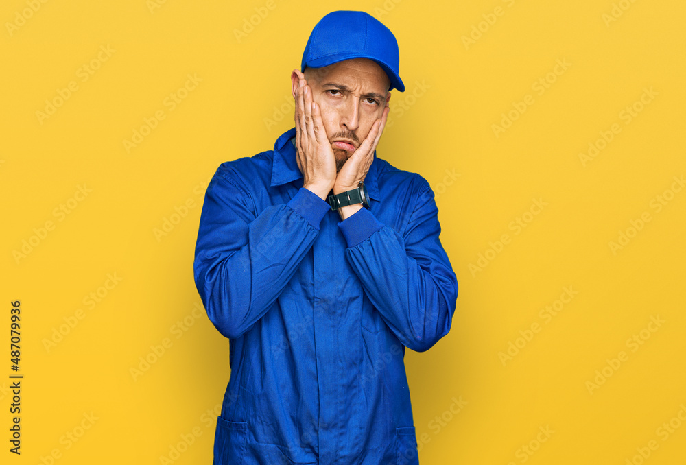 Bald man with beard wearing builder jumpsuit uniform tired hands covering face, depression and sadness, upset and irritated for problem