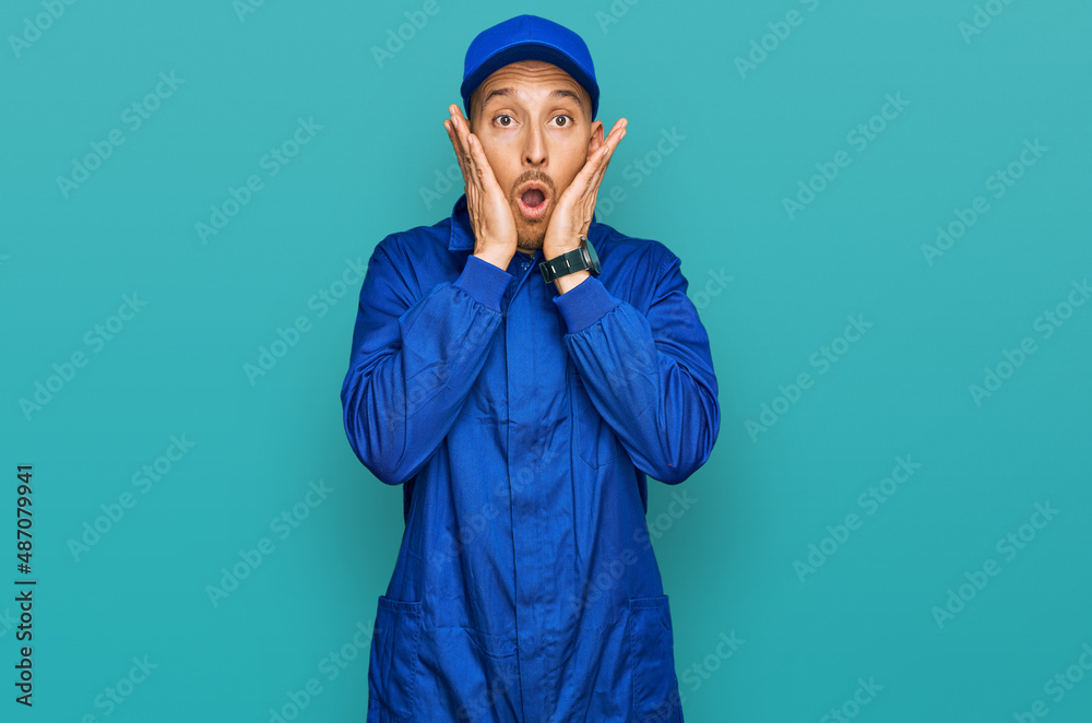 Bald man with beard wearing builder jumpsuit uniform afraid and shocked, surprise and amazed expression with hands on face Bald man with beard wearing builder jumpsuit uniform afraid and shocked, surprise and amazed expression with hands on face