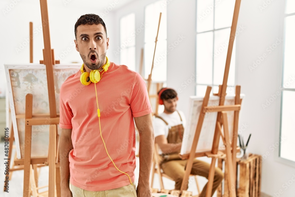 Young hispanic man at art studio afraid and shocked with surprise expression, fear and excited face. Young hispanic man at art studio afraid and shocked with surprise expression, fear and excited face.