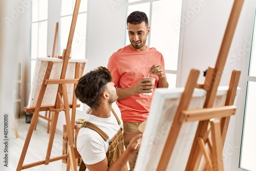 Two hispanic men couple smiling confident drinking coffee and drawing at art studio