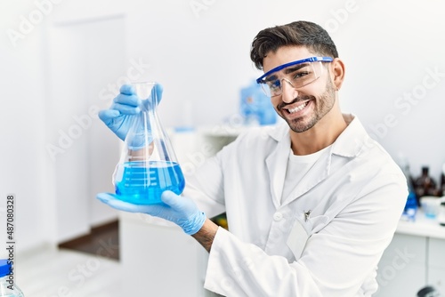 Handsome hispanic man working as scientific holding erlenmeyer flask at laboratory