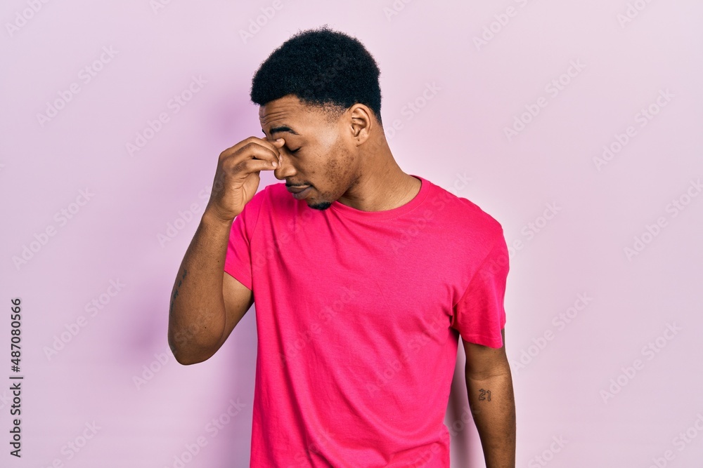 Young african american man wearing casua t shirt tired rubbing nose and eyes feeling fatigue and headache. stress and frustration concept. Young african american man wearing casua t shirt tired rubbing nose and eyes feeling fatigue and headache. stress and frustration concept.