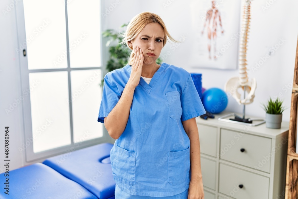 Beautiful blonde physiotherapist woman working at pain recovery clinic touching mouth with hand with painful expression because of toothache or dental illness on teeth. dentist Beautiful blonde physiotherapist woman working at pain recovery clinic touching mouth with hand with painful expression because of toothache or dental illness on teeth. dentist