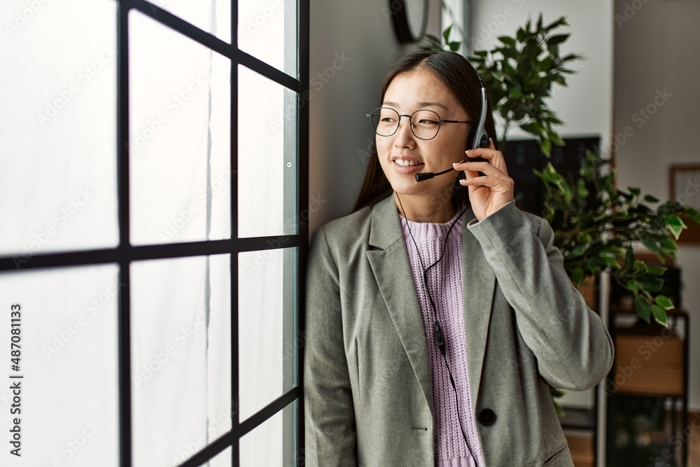 Young chinese call center agent woman smiling happy standing at the office. Young chinese call center agent woman smiling happy standing at the office.