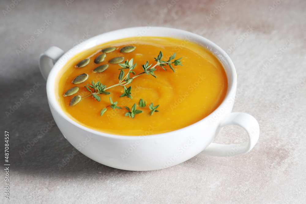 Vegetarian pumpkin soup with herbs in a white ceramic bowl on a light gray background close-up Vegetarian pumpkin soup with herbs in a white ceramic bowl on a light gray background close-up