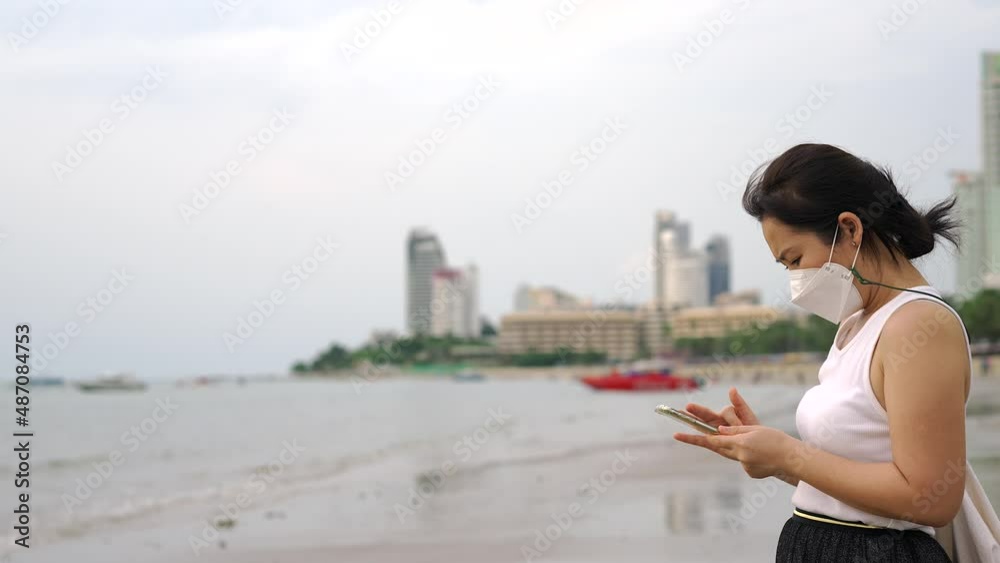 Young Woman wearing a protective face mask standing on a beach using mobile phone. Young Woman wearing a protective face mask standing on a beach using mobile phone.