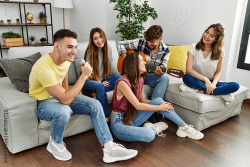 Group of young friends on party playing classical guitar and singing song at home.