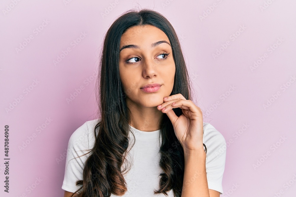 Young hispanic woman wearing casual white t shirt serious face thinking about question with hand on chin, thoughtful about confusing idea Young hispanic woman wearing casual white t shirt serious face thinking about question with hand on chin, thoughtful about confusing idea