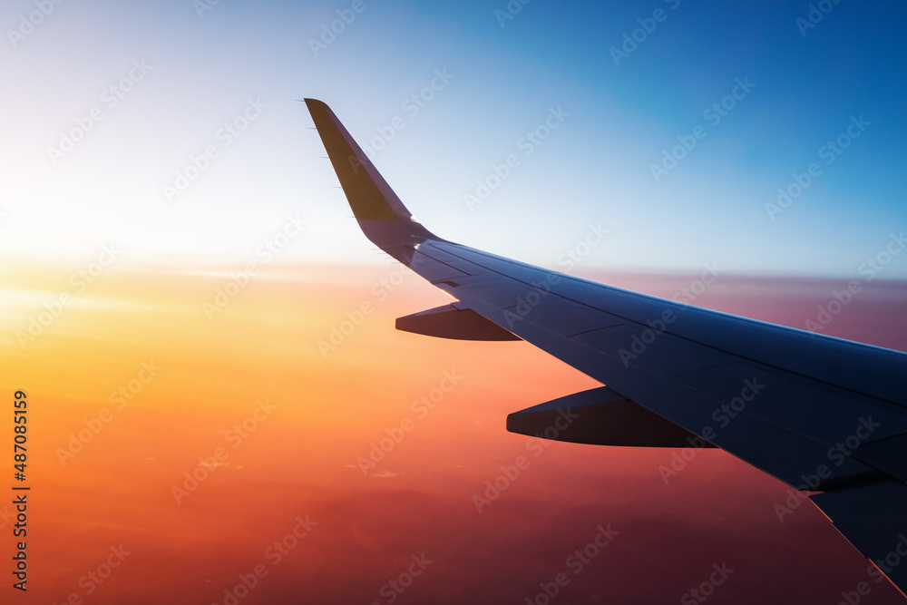 View from the window of the aircraft on the wing over the colorful sunset and illuminated vivid clouds