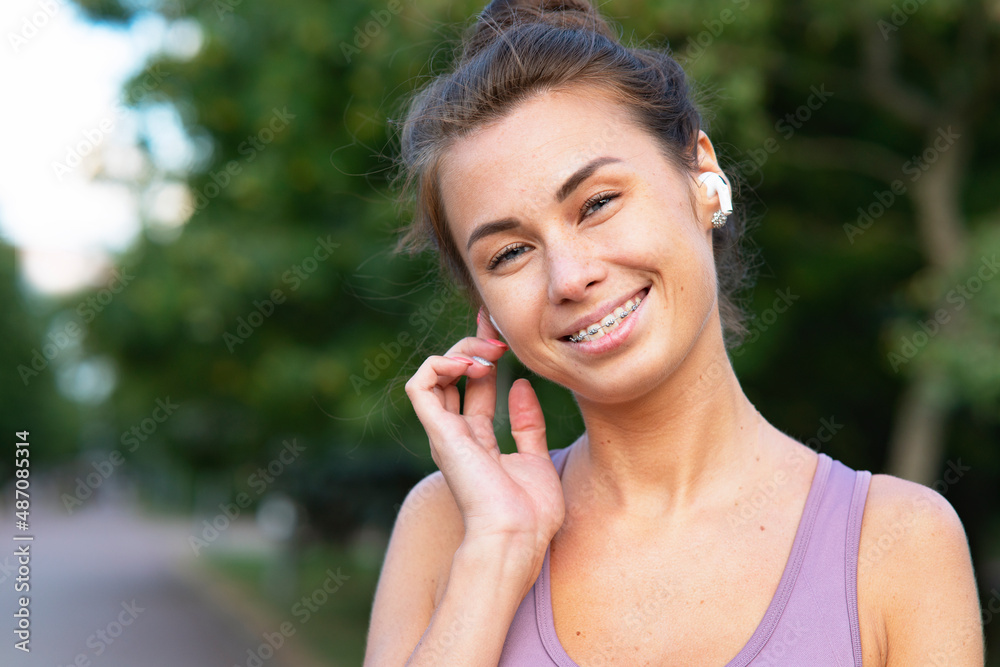 Portrait of beautiful, happy young woman talking through bluetooth headphones while at sports jog. A girl laughs, listens to music with, bluetooth wireless headphones. Funny mask with braces on teeth Portrait of beautiful, happy young woman talking through bluetooth headphones while at sports jog. A girl laughs, listens to music with, bluetooth wireless headphones. Funny mask with braces on teeth