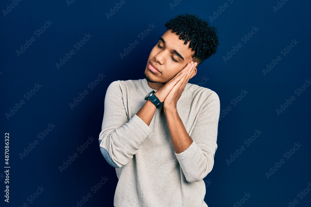 Young african american man wearing casual clothes sleeping tired dreaming and posing with hands together while smiling with closed eyes.