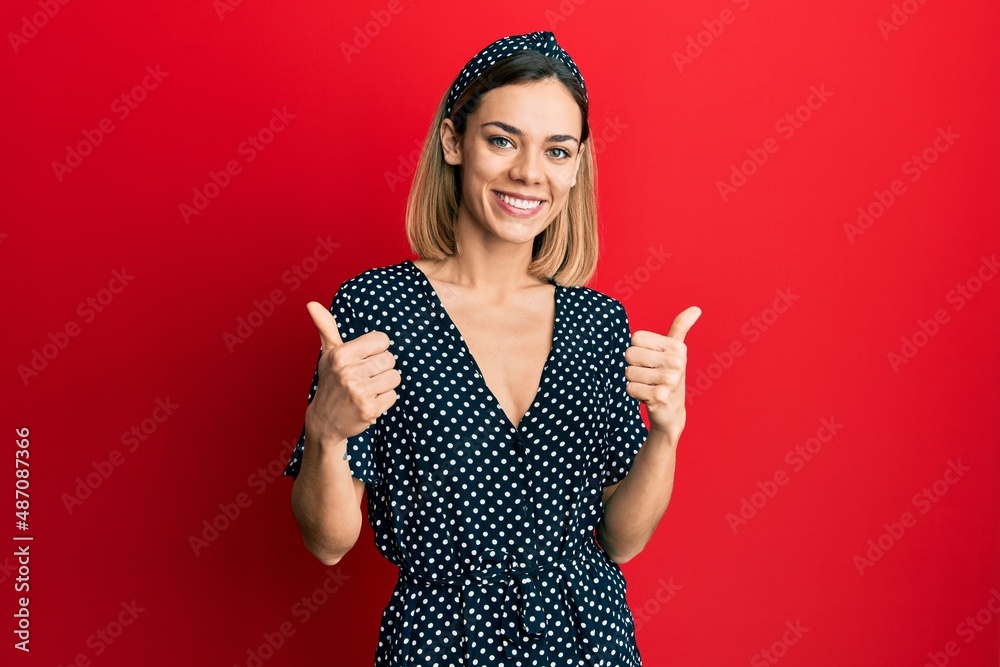 Young caucasian blonde woman wearing beautiful black and white dress success sign doing positive gesture with hand, thumbs up smiling and happy. cheerful expression and winner gesture.